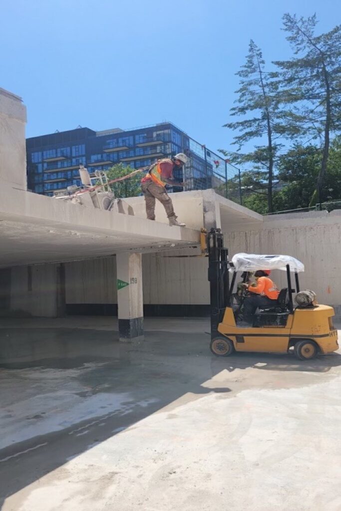 Blackcore Environmental - A construction worker stands on a ledge while a forklift with another worker lifts a concrete mixer to the upper level of a building under construction.