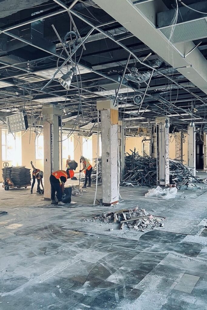 Blackcore Environmental - Construction workers in safety vests clear debris inside a partially demolished building with exposed ceiling wires and scattered rubble.