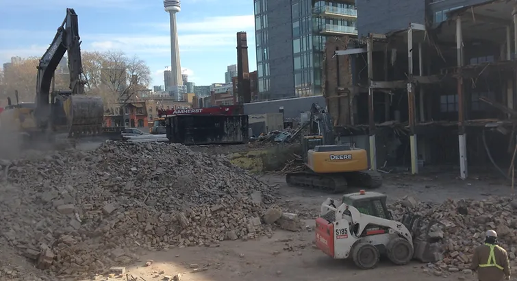 Blackcore Environmental - Construction site with rubble piles, several diggers, and a worker in a safety vest; city buildings and a tall tower are visible in the background.