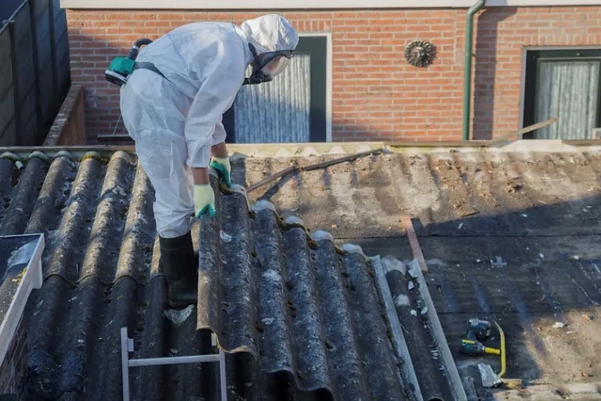 Blackcore Environmental - Person in protective gear removes corrugated asbestos roofing sheets from a building, with tools and equipment visible on the roof.