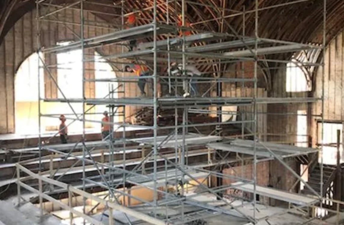 Blackcore Environmental - Construction workers standing on scaffolding inside a large, unfinished building with arched ceilings and exposed beams.