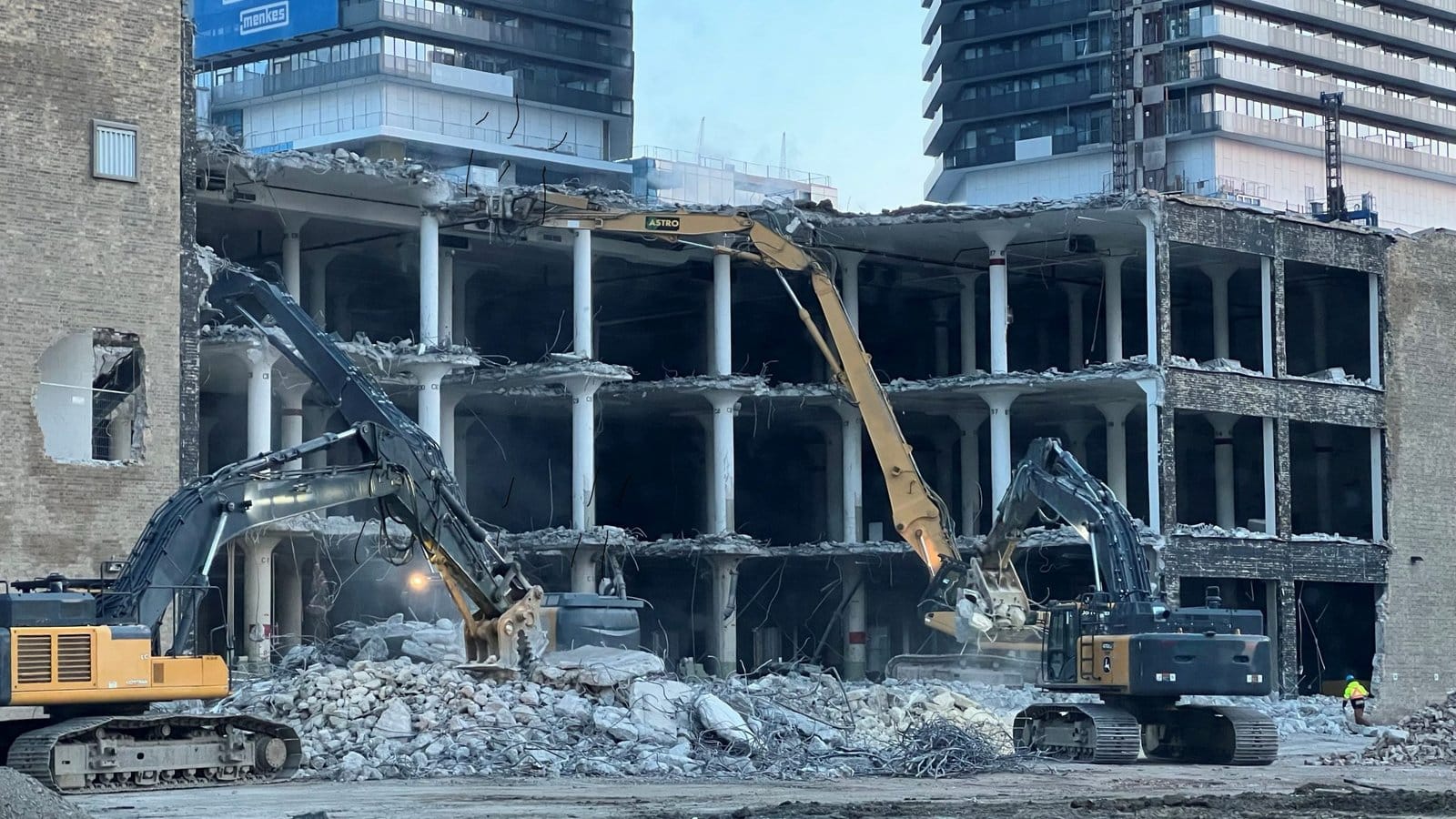 Blackcore Environmental - Two diggers demolishing a multi-storey concrete building, with debris and rubble scattered in the foreground and modern buildings in the background.