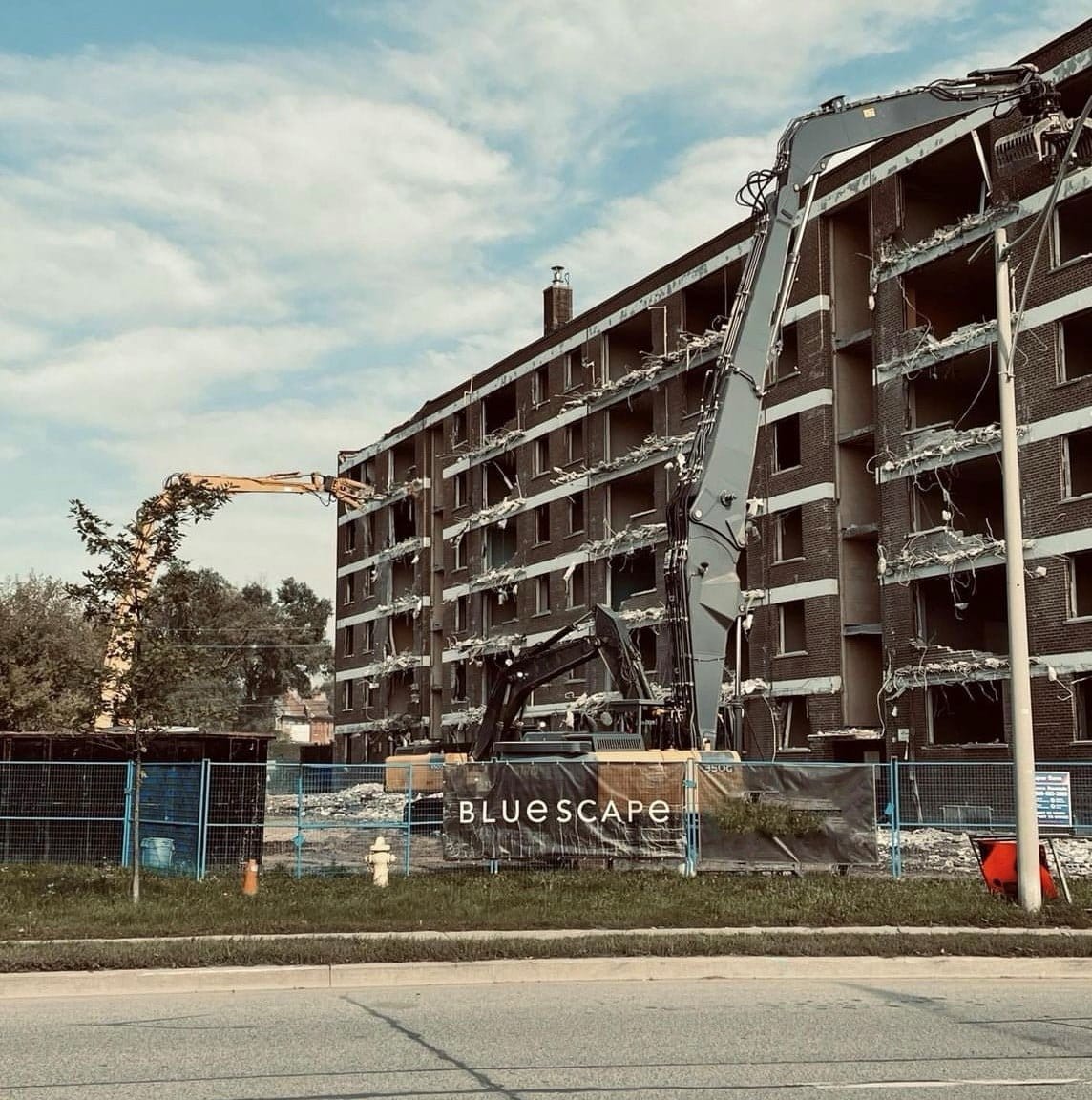 Blackcore Environmental - Construction machinery demolishing a multi-storey building behind a fence with a BLUESCAPE sign; debris and exposed floors visible.