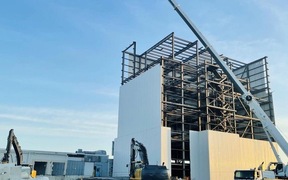 Blackcore Environmental - A construction site with a steel building frame partially covered by white panels, several cranes, and excavators visible under a clear sky.