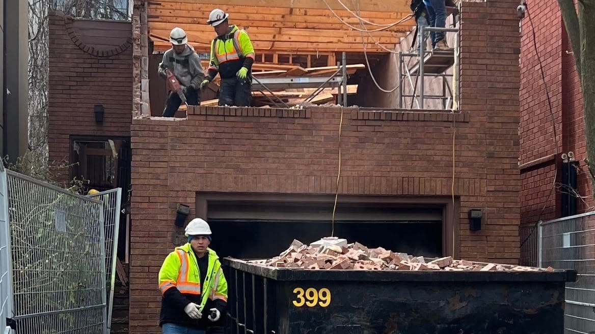 Blackcore Environmental - Three construction workers in safety gear demolish the upper floor of a brick building, with debris being thrown into a skip labelled 399.
