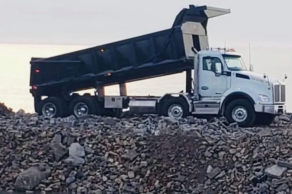 Blackcore Environmental - A white tipper lorry with its bed raised is unloading rocks onto a rocky construction site.